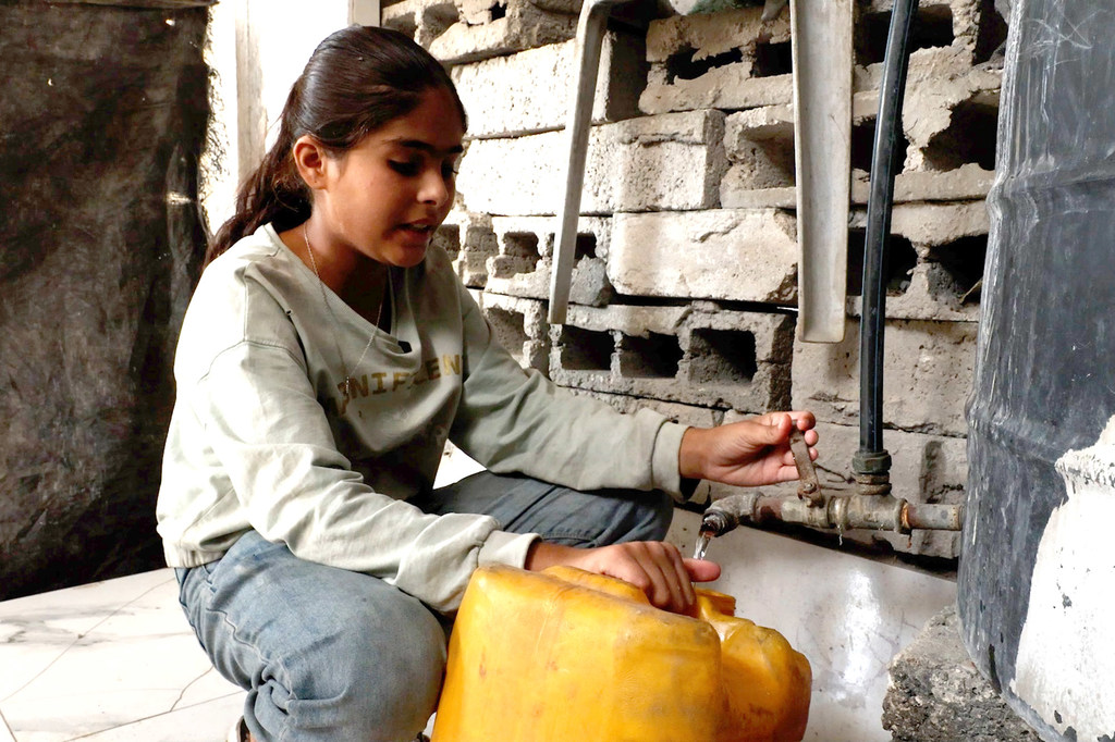 Selin Al-Dada, una niña de Gaza, llena un galón de plástico con agua potable.